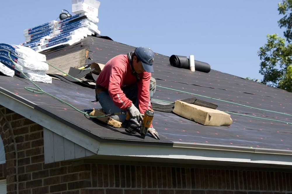 A worker on a rooftop, actively repairing with tools to maintain the roof's condition.