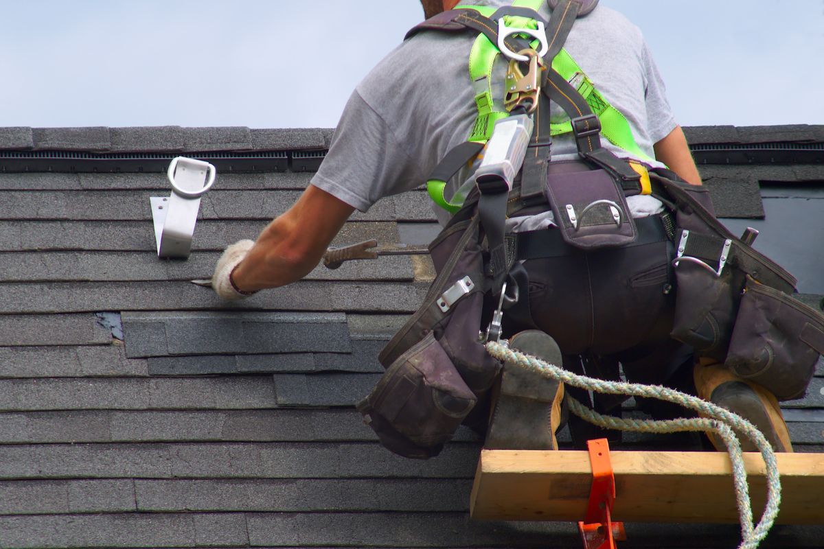 A man climbs a ladder to work on a roof, wearing safety gear and focused on his task.
